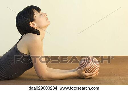 Picture - Woman lying on stomach, holding ball, eyes closed, side view. Fotosearch