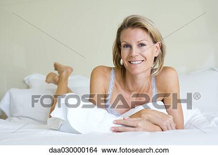 Woman lying on stomach in bed, smiling at camera View Large Photo Image Picture - Woman lying on stomach in bed, smiling at camera. Fotosearch