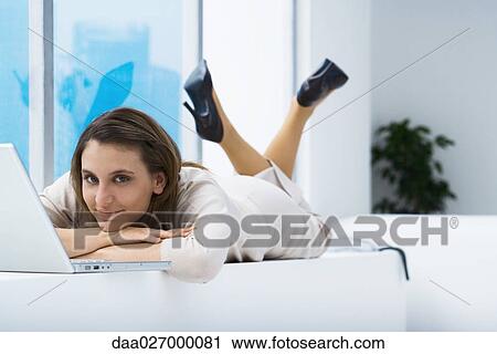 Woman lying on stomach near laptop, smiling at camera View Large Photo Image Stock Image - Woman lying on stomach near laptop, smiling at camera. Fotosearch