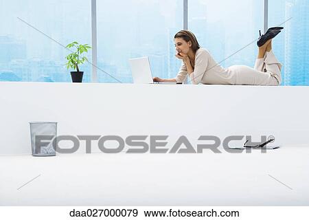 Woman lying on stomach next to window, using laptop, full length View Large Photo Image Stock Photo - Woman lying on stomach next to window, using laptop, full length. Fotosearch