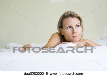 Stock Photograph - Woman lying on stomach on bed, looking away. Fotosearch