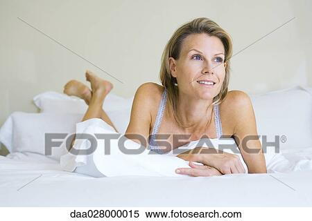 Woman lying on stomach on bed, looking away, smiling View Large Photo Image Stock Photography - Woman lying on stomach on bed, looking away, smiling. Fotosearch