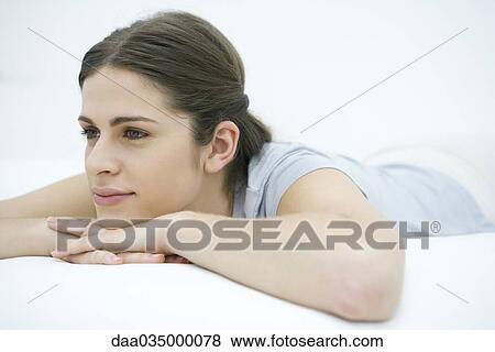 Stock Photo - Woman lying on stomach, resting head on arms, looking away. Fotosearch