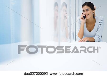 Stock Image - Woman lying on stomach, using cell phone. Fotosearch
