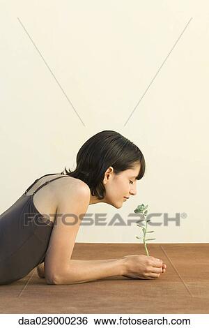 Stock Photograph - Woman lying on the ground, smelling jade plant, eyes closed, side view. Fotosearch