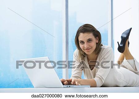 Woman lying on windowsill, using laptop, smiling at camera View Large Photo Image Stock Image - Woman lying on windowsill, using laptop, smiling at camera. Fotosearch