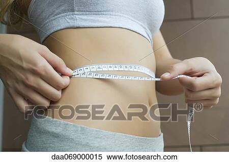 Stock Photography - Woman measuring her waist with measuring tape, cropped. Fotosearch