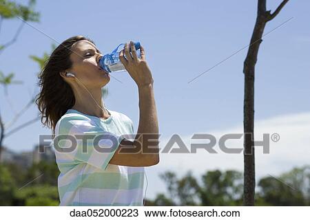 Stock Image - Woman outdoors, drinking water from bottle. Fotosearch