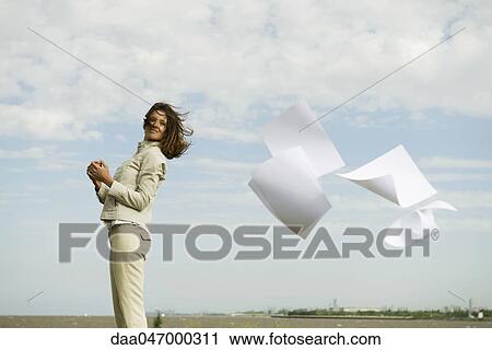 Woman outdoors smiling, watching documents caught in wind fly away View Large Photo Image Stock Image - Woman outdoors smiling, watching documents caught in wind fly away. Fotosearch