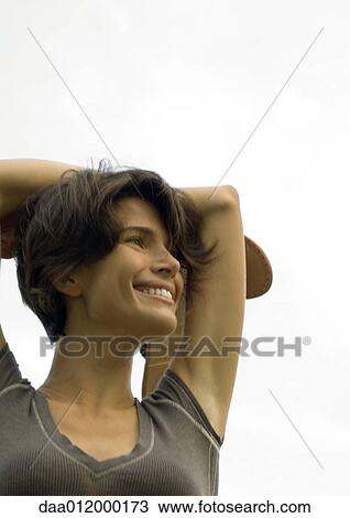 Stock Image - Woman outdoors with arms behind head, holding shoes in hand. Fotosearch
