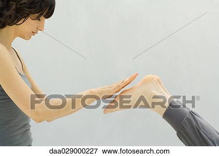 Stock Photo - Woman performing reiki massage on person's feet, side view. Fotosearch