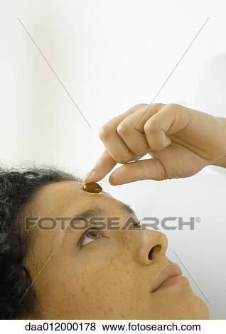 Stock Photo - Woman placing glass pebble on forehead. Fotosearch