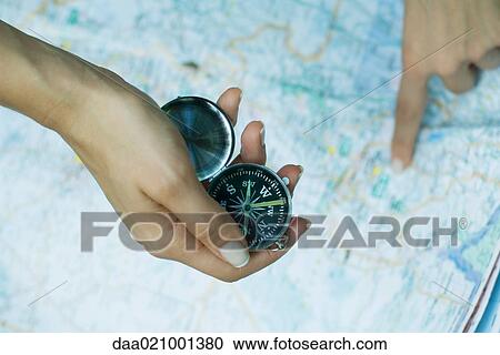 Stock Image - Woman pointing to map and holding compass, close-up. Fotosearch