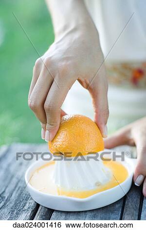 Stock Photograph - Woman pressing orange with citrus press, close-up, cropped view of hands. Fotosearch