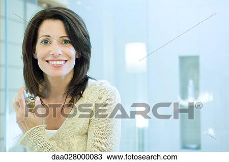 Woman putting on perfume in bathroom, smiling at camera View Large Photo Image Stock Image - Woman putting on perfume in bathroom, smiling at camera. Fotosearch
