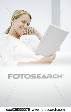 Stock Photograph - Woman reading book, sitting on sofa. Fotosearch