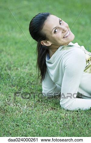 Stock Image - Woman reclining on grass, smiling over shoulder at camera. Fotosearch