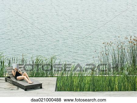 Woman reclining on lounge chair, reading, next to lake View Large Photo Image Stock Photo - Woman reclining on lounge chair, reading, next to lake. Fotosearch