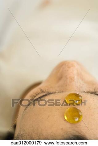 Stock Photo - Woman reclining with two glass pebbles on forehead, close-up. Fotosearch
