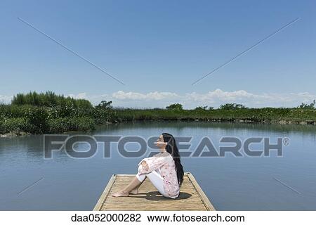 Stock Image - Woman relaxing on dock with eyes closed. Fotosearch
