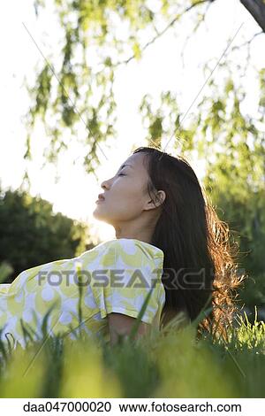 Stock Image - Woman relaxing on grass with eyes closed. Fotosearch