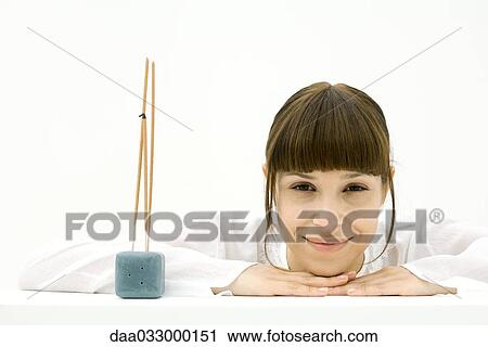 Woman resting head on arms beside incense, smiling at camera View Large Photo Image Stock Image - Woman resting head on arms beside incense, smiling at camera. Fotosearch