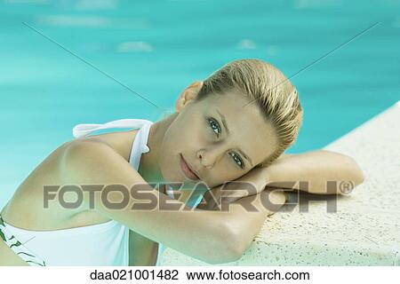 Stock Image - Woman resting head on edge of pool, looking at camera. Fotosearch