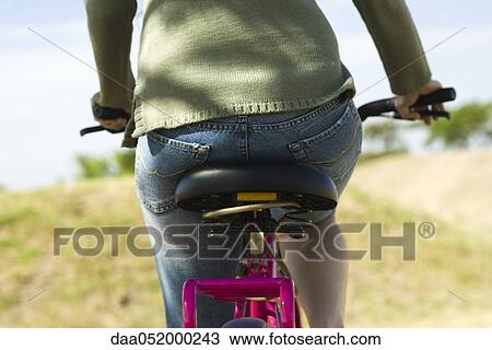 Stock Image - Woman riding bicycle, cropped rear view. Fotosearch