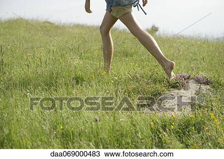 Stock Image - Woman running on meadow with bare feet, low section. Fotosearch