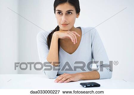 Woman sitting at table with hand under chin, looking away View Large Photo Image Stock Photo - Woman sitting at table with hand under chin, looking away. Fotosearch