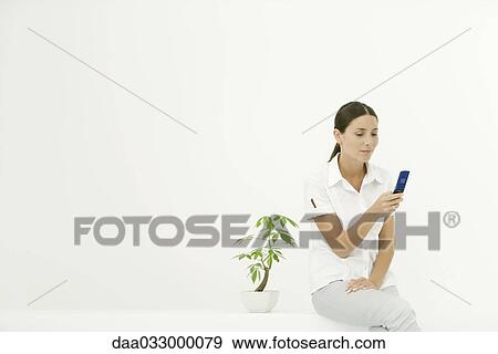 Woman sitting beside potted plant, using cell phone View Large Photo Image Stock Photo - Woman sitting beside potted plant, using cell phone. Fotosearch