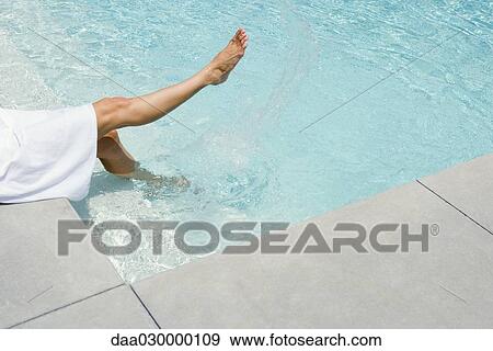 Woman sitting beside swimming pool, splashing water with feet, cropped view View Large Photo Image Stock Photo - Woman sitting beside swimming pool, splashing water with feet, cropped view. Fotosearch