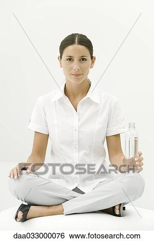 Woman sitting cross-legged, holding water bottle, smiling at camera View Large Photo Image Stock Photograph - Woman sitting cross-legged, holding water bottle, smiling at camera. Fotosearch