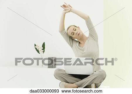 Woman sitting cross-legged in office, stretching, laptop computer on her lap View Large Photo Image Stock Image - Woman sitting cross-legged in office, stretching, laptop computer on her lap. Fotosearch