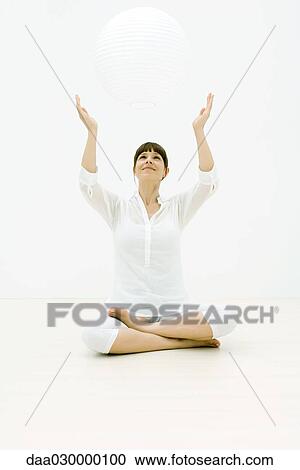 Woman sitting cross-legged on the ground with arms raised, looking up at sphere View Large Photo Image Stock Image - Woman sitting cross-legged on the ground with arms raised, looking up at sphere. Fotosearch