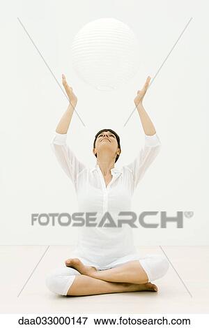 Woman sitting cross-legged on the ground with arms raised, looking up at sphere View Large Photo Image Stock Photo - Woman sitting cross-legged on the ground with arms raised, looking up at sphere. Fotosearch