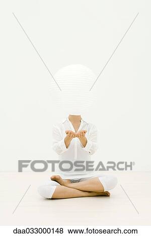 Stock Photo - Woman sitting cross-legged on the ground, paper lantern floating in front of her face. Fotosearch