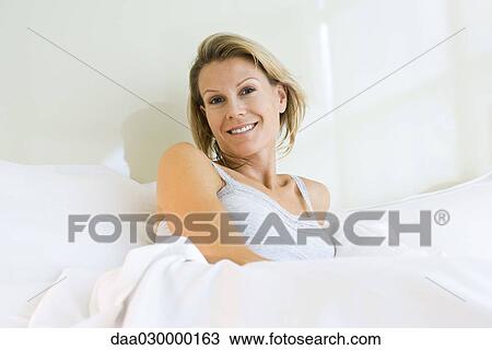 Woman sitting in bed, smiling at camera View Large Photo Image Stock Image - Woman sitting in bed, smiling at camera. Fotosearch
