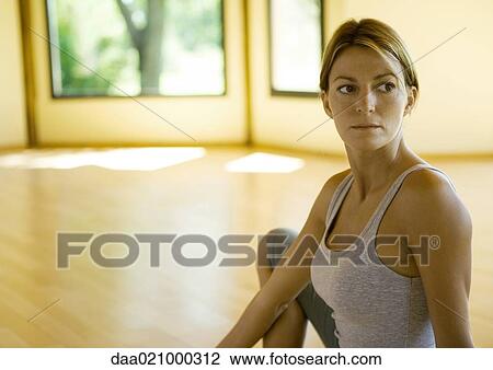 Stock Image - Woman sitting in exercise studio, looking away. Fotosearch
