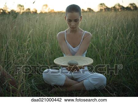 Woman sitting in field, holding out dish with stone in center View Large Photo Image Stock Image - Woman sitting in field, holding out dish with stone in center. Fotosearch