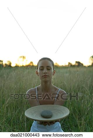 Woman sitting in field, holding out dish with stone in center View Large Photo Image Stock Image - Woman sitting in field, holding out dish with stone in center. Fotosearch
