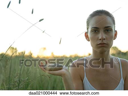 Woman sitting in field, holding stone in hand View Large Photo Image Picture - Woman sitting in field, holding stone in hand. Fotosearch