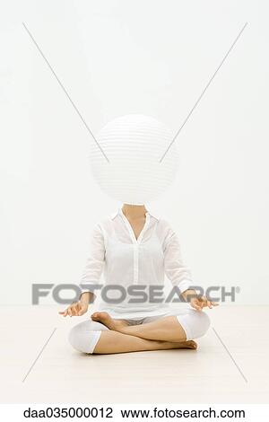 Stock Image - Woman sitting in lotus position, paper lantern obscuring face. Fotosearch