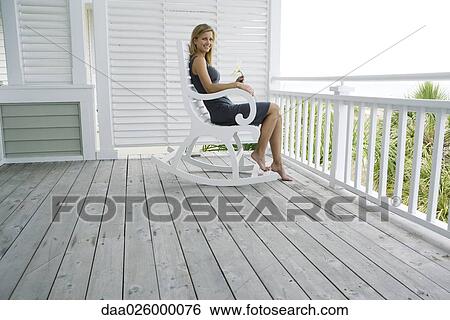 Woman sitting in rocking chair on porch, holding flower, smiling at camera View Large Photo Image Stock Photograph - Woman sitting in rocking chair on porch, holding flower, smiling at camera. Fotosearch