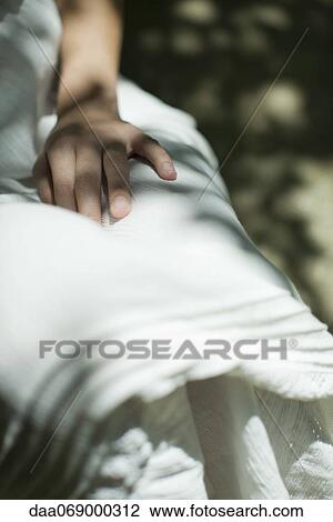 Stock Image - Woman sitting in shadow, mid section. Fotosearch