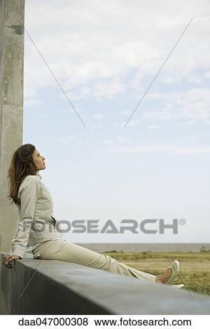 Woman sitting on a ledge looking at view, daydreaming View Large Photo Image Stock Photo - Woman sitting on a ledge looking at view, daydreaming. Fotosearch