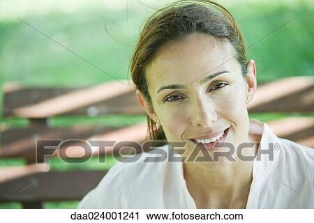 Woman sitting on bench, smiling at camera, portrait View Large Photo Image Stock Image - Woman sitting on bench, smiling at camera, portrait. Fotosearch