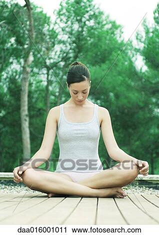 Stock Image - Woman sitting on deck in indian style, head down. Fotosearch