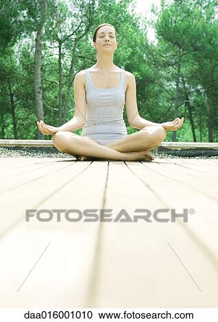 Stock Image - Woman sitting on deck, in lotus position. Fotosearch