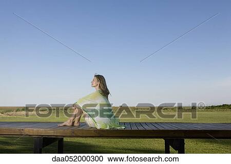 Stock Image - Woman sitting on deck wrapped in scarf, looking away in thought. Fotosearch